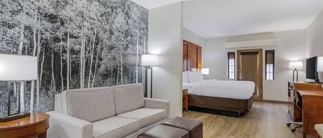 A hotel room with a sofa, a bed, a desk, and a large wall mural.