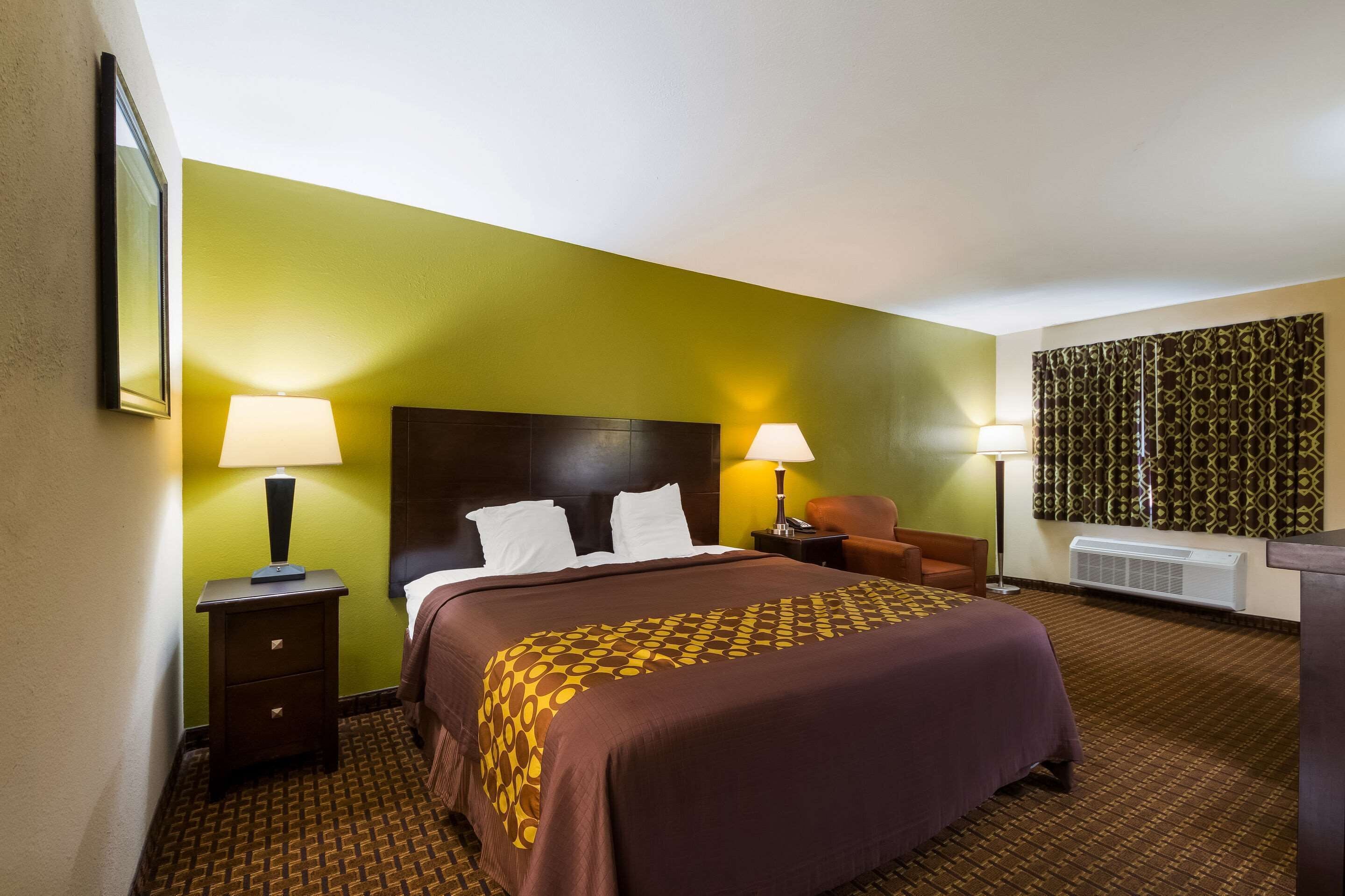 A hotel room with a large bed, two bedside tables with lamps, a chair, and a patterned wall.