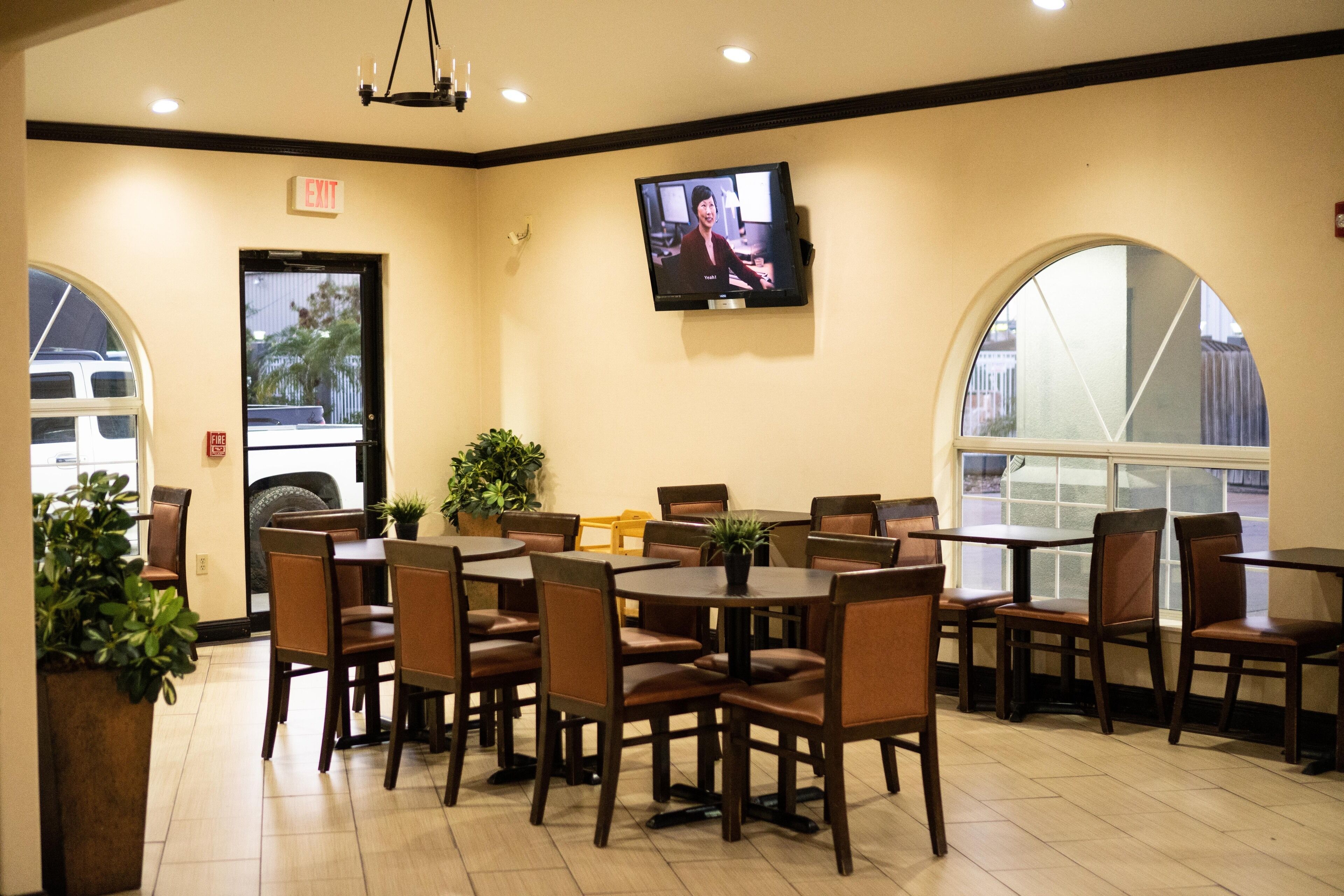 Un restaurante con varias mesas y sillas, un televisor en la pared y un amplio ventanal con vistas al exterior.