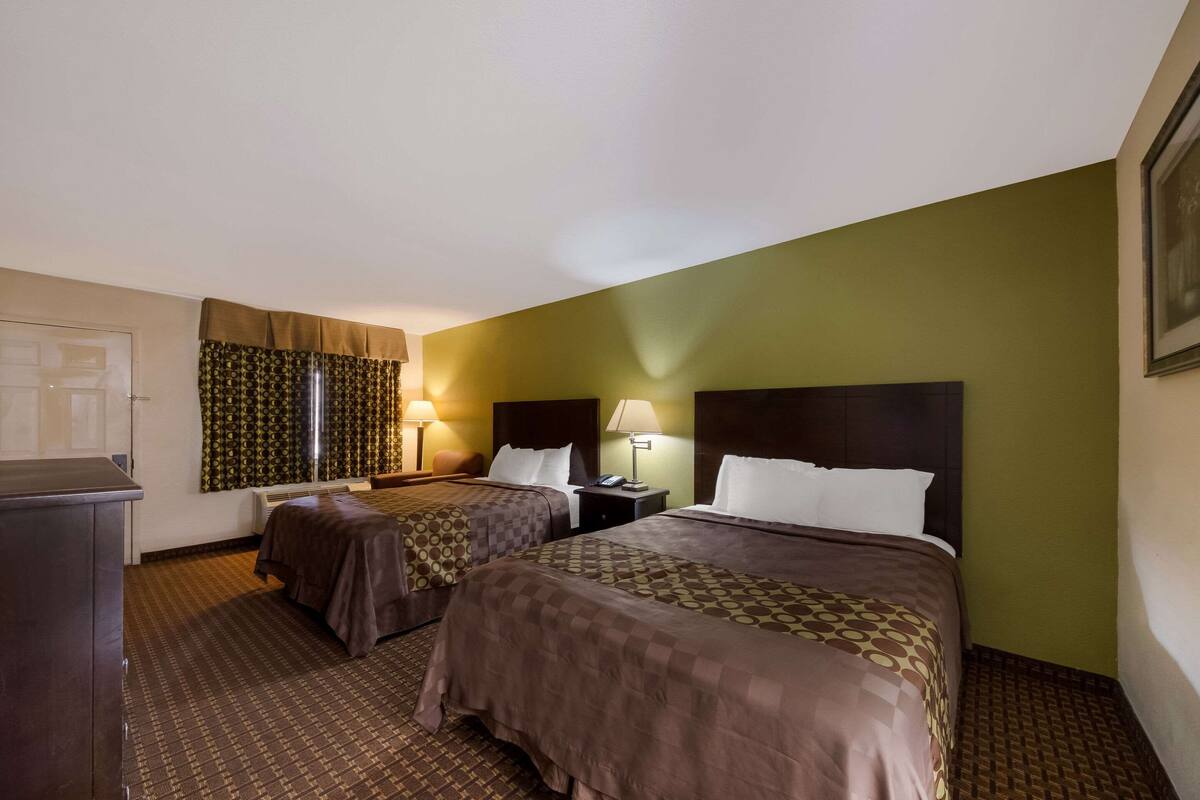 A hotel room with two beds, a desk, a chair, a lamp, and a window with curtains.