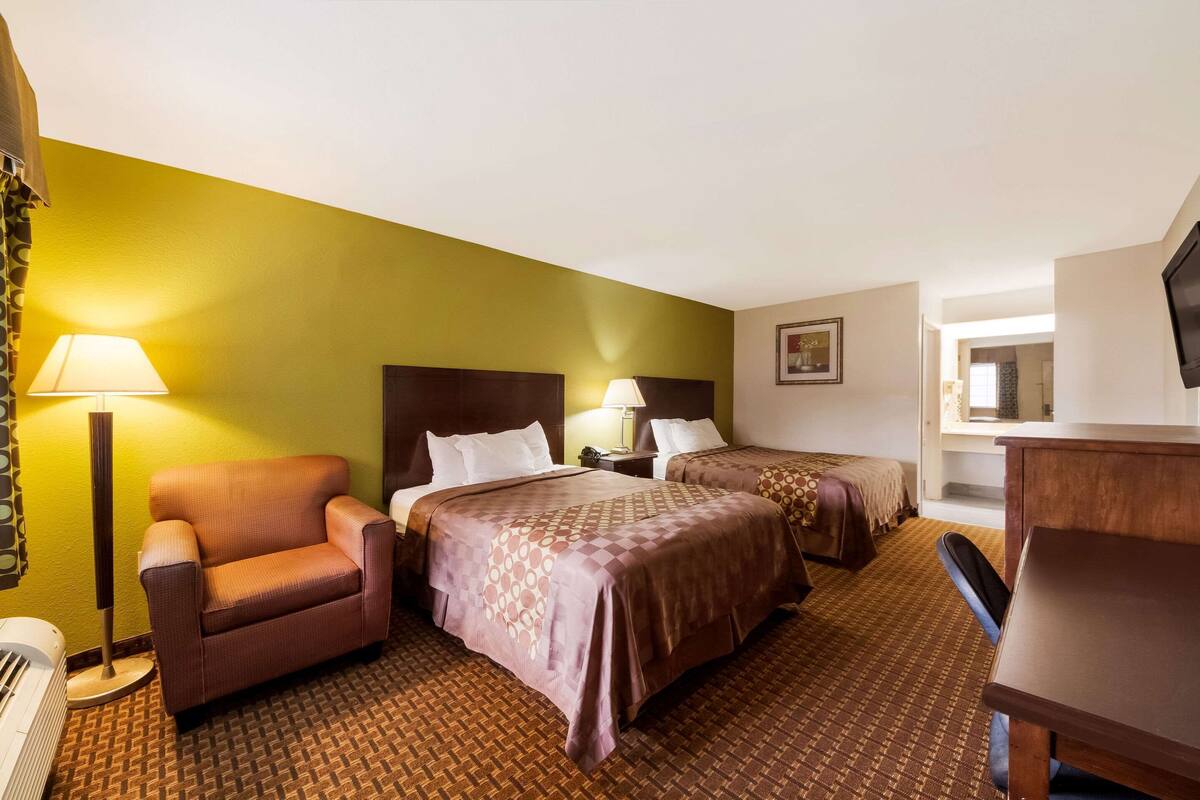 A hotel room with two beds, a chair, a desk, and a television.
