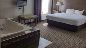 A hotel room with a large bed, a flat-screen TV mounted on the wall, a bathroom with a bathtub, and a window with curtains. - Baymont by Wyndham Auburn (Auburn)