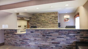 A reception desk with a stone facade, a sign reading 'Baymont,' and a poster on the wall. - Baymont by Wyndham Auburn (Auburn)