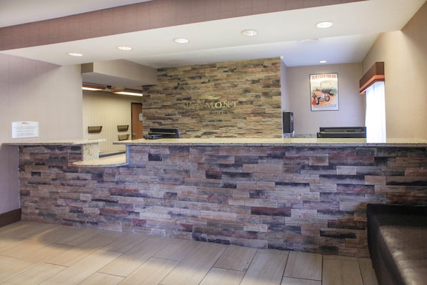 A reception desk with a stone facade, a sign reading 'Baymont,' and a poster on the wall.