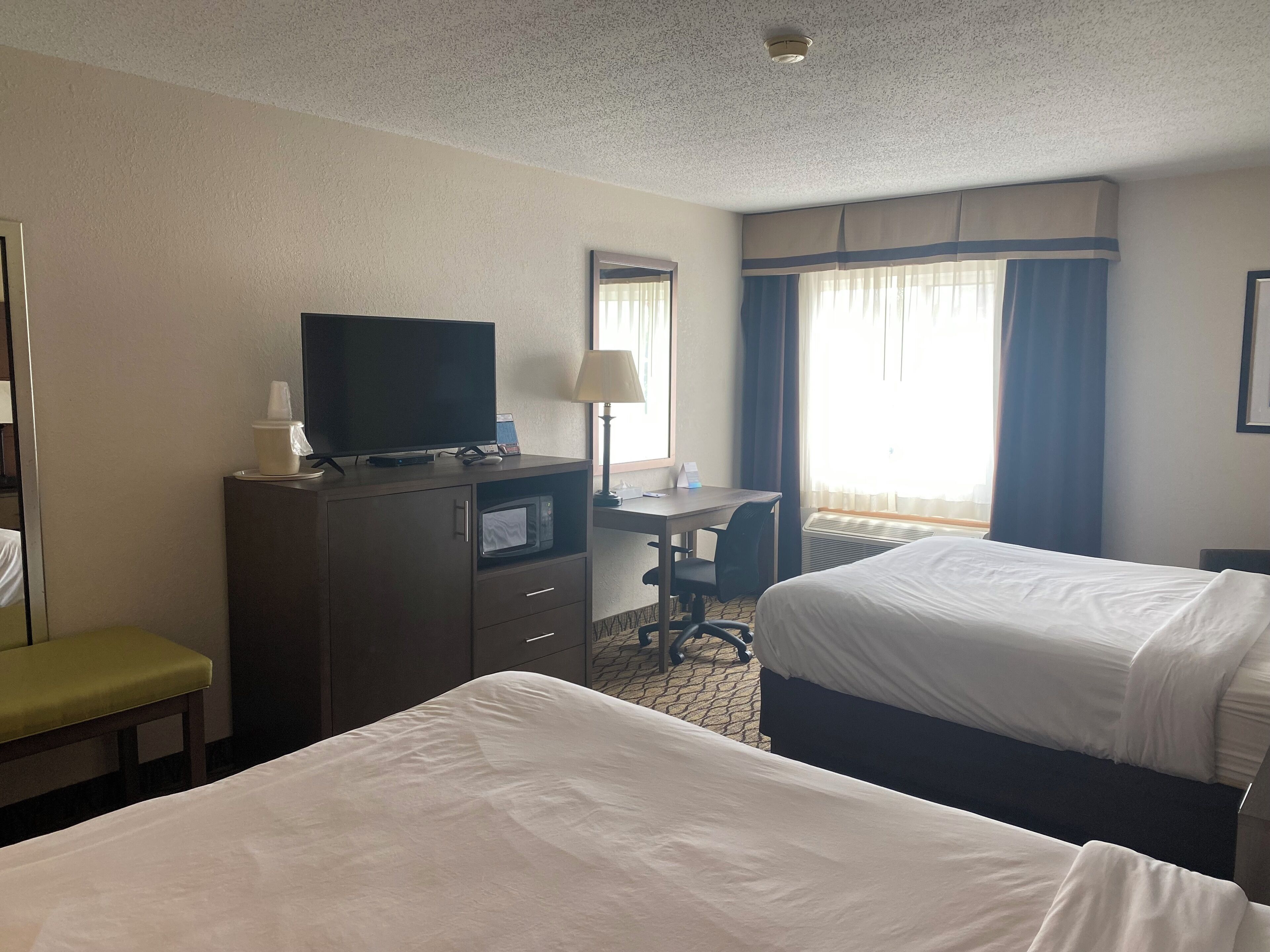A hotel room with two beds, a desk with a chair, a television on a dresser, and a window with curtains.