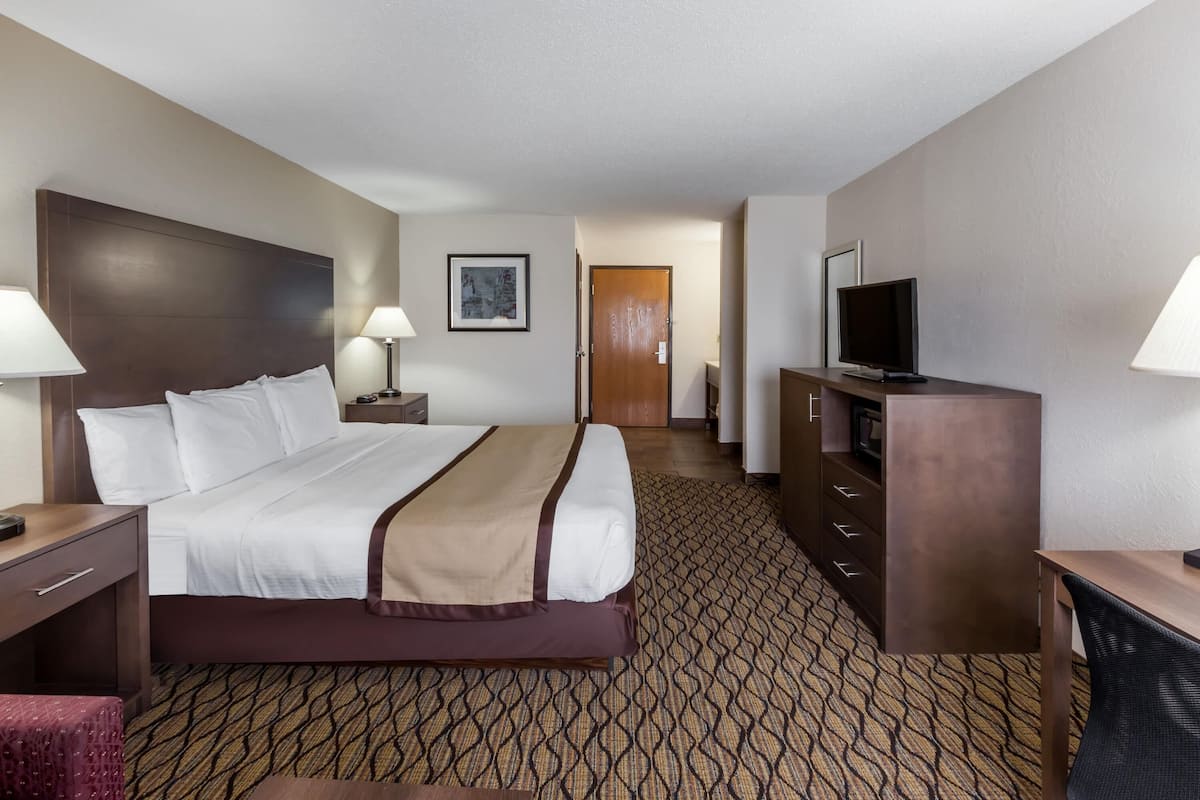 A hotel room with a large bed, bedside tables, a TV, a desk, and a patterned carpet.