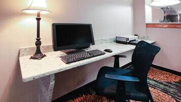 A hotel room with a desk, computer, keyboard, mouse, and a chair.