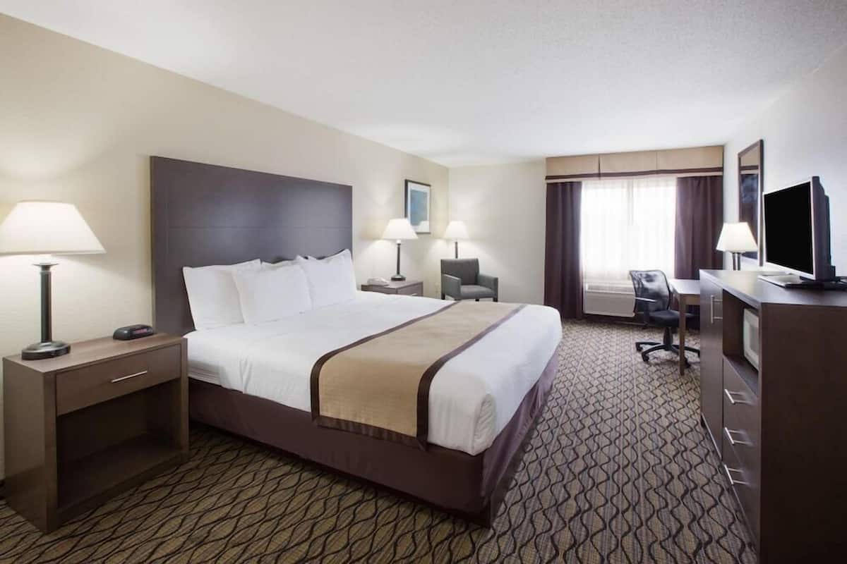 A hotel room with a large bed, two bedside tables with lamps, a desk with a chair, a television, and a window with curtains.