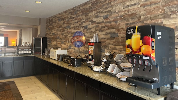 A breakfast area with a stone wall, a coffee machine, and a sign for the breakfast corner. - Baymont by Wyndham Auburn (Auburn)