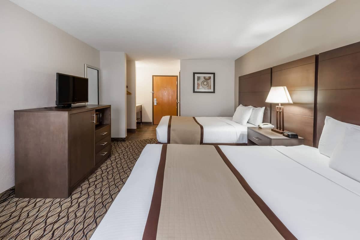 A hotel room with two beds, a TV, a desk with a lamp, and a door leading to a bathroom.