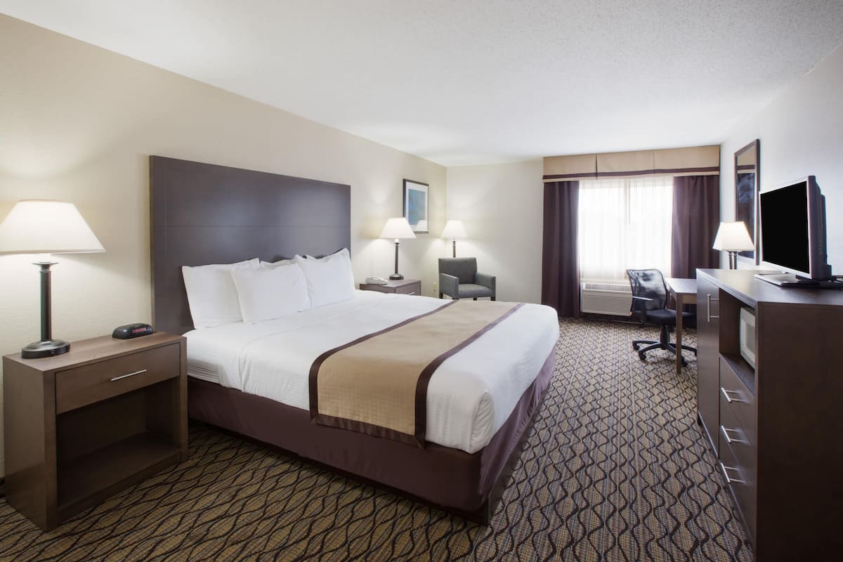 A hotel room with a large bed, two bedside tables with lamps, a desk with a chair, a television, and a window with curtains.