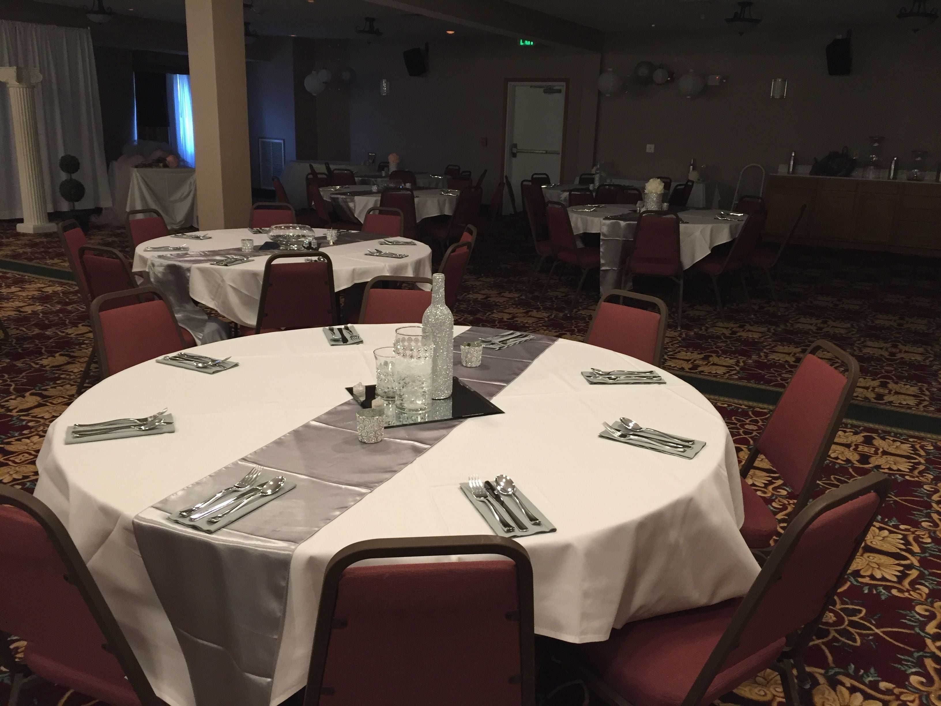 Une salle de banquet avec des tables rondes dressées pour le repas, chacune étant recouverte d’une nappe blanche, entourée de chaises rouges et agrémentée de couverts en argent.