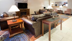 A modern living room with leather sofas, a flat-screen TV, and a fireplace. - Baymont by Wyndham Auburn (Auburn)