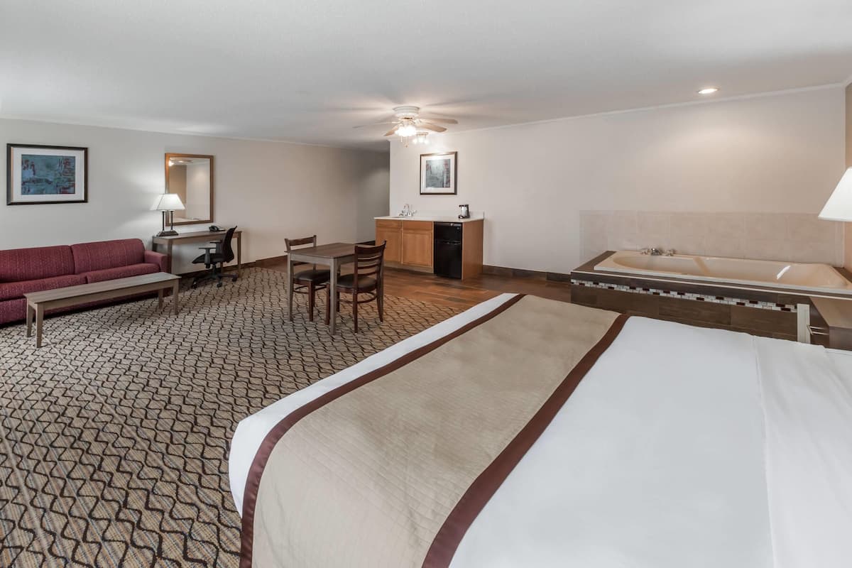 A hotel room with a bed, a desk, a chair, a sofa, a small kitchenette, and a bathroom.