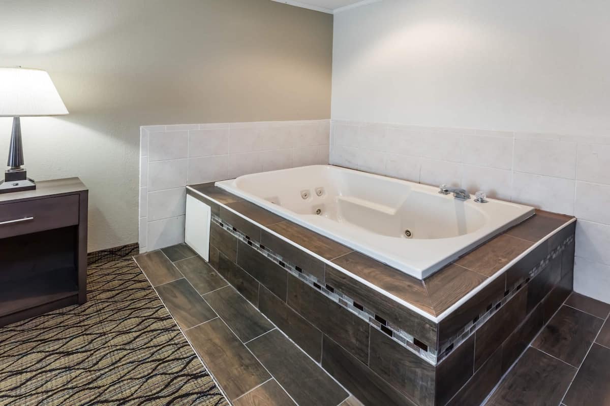 A modern bathroom with a freestanding bathtub, a nightstand with a lamp, and a patterned rug.