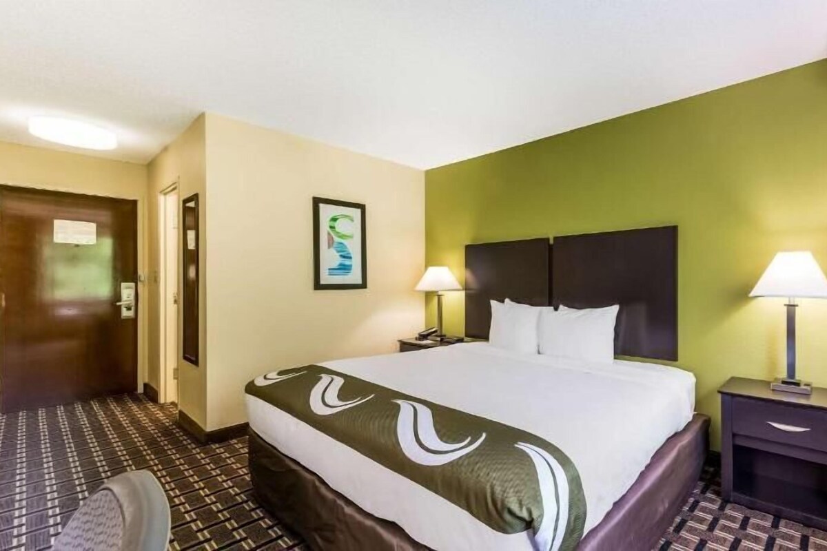 Une chambre d’hôtel avec un lit, deux tables de chevet avec des lampes, une porte et un mur orné d’un tableau.