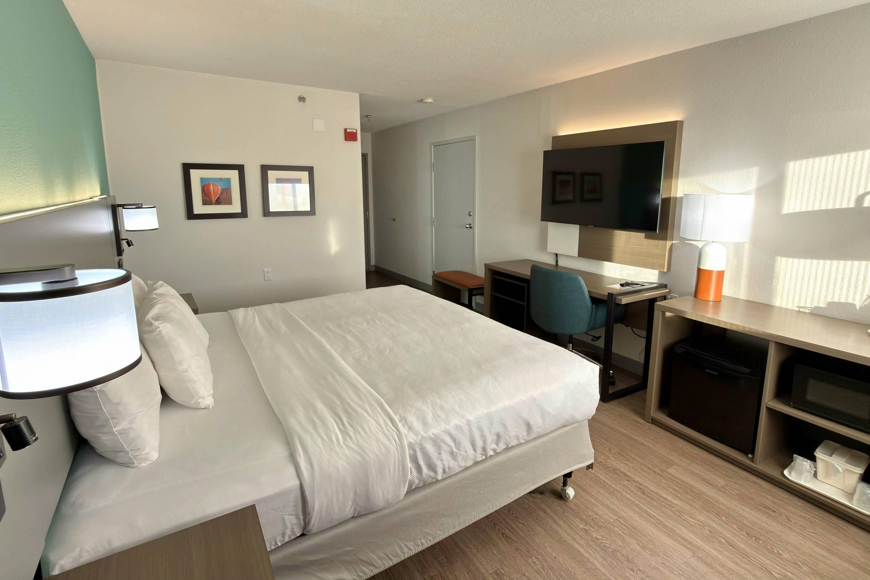 Habitación de hotel con cama, escritorio, silla, televisión y un pequeño rincón de estar.