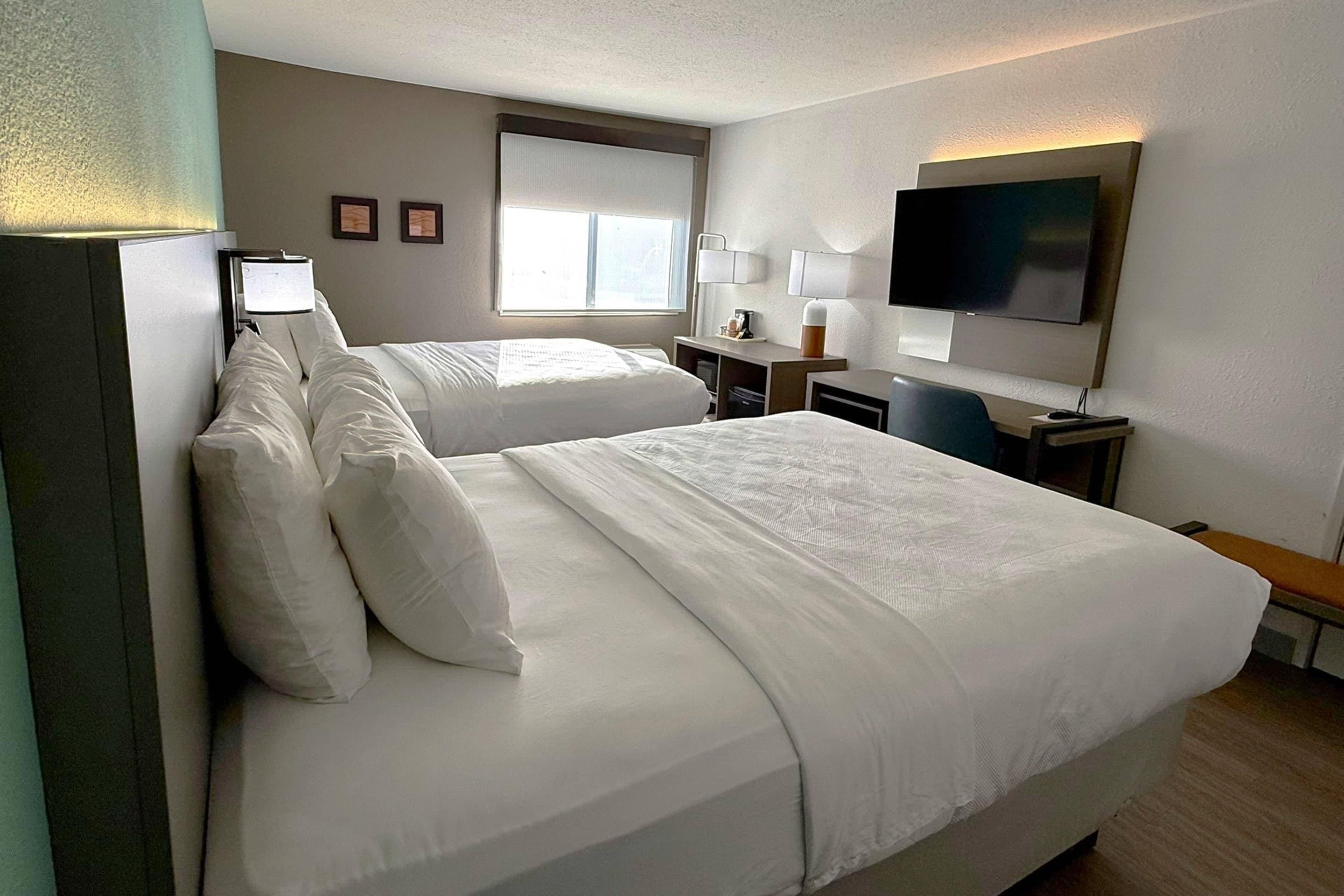 Une chambre d’hôtel avec deux lits, un bureau, une télévision et une fenêtre.