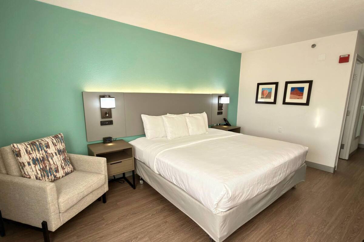 Hotellihuone, jossa on suuri sänky, yöpöytä, tuoli ja pieni sivupöytä.