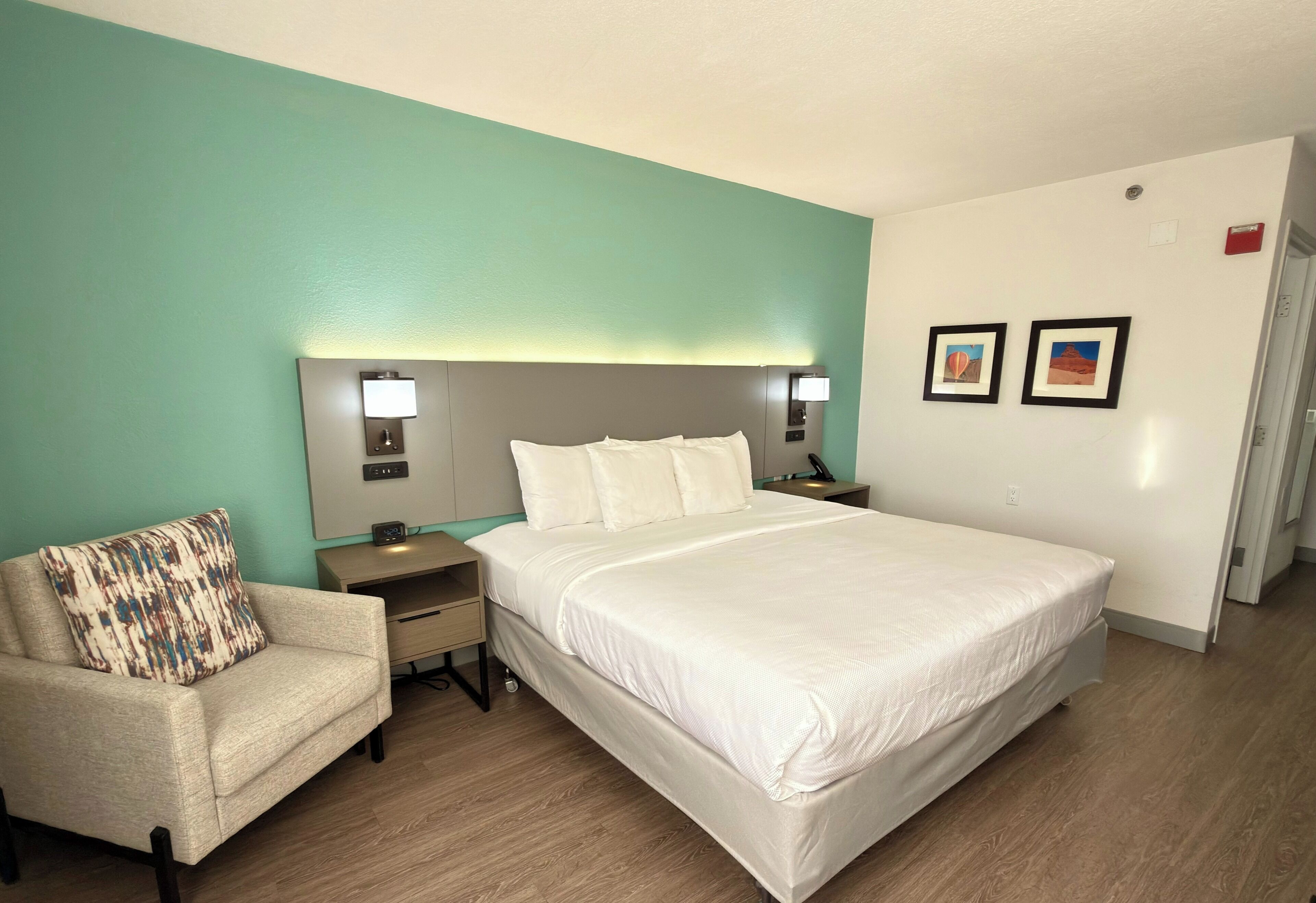 A hotel room with a bed, a chair, a nightstand, and two wall-mounted lamps.