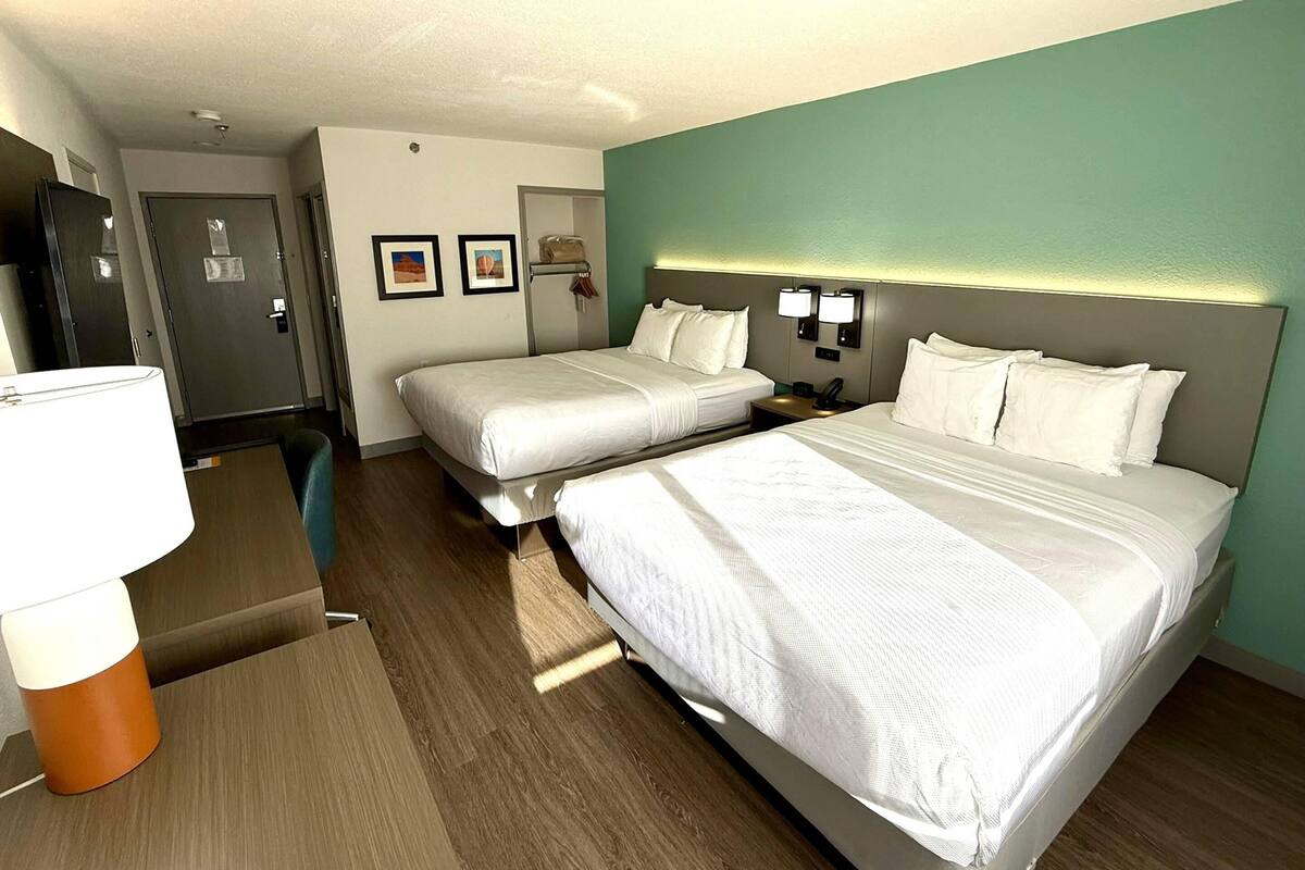 Hotellihuone, jossa on kaksi sänkyä, työpöytä, tuoli ja lamppu.