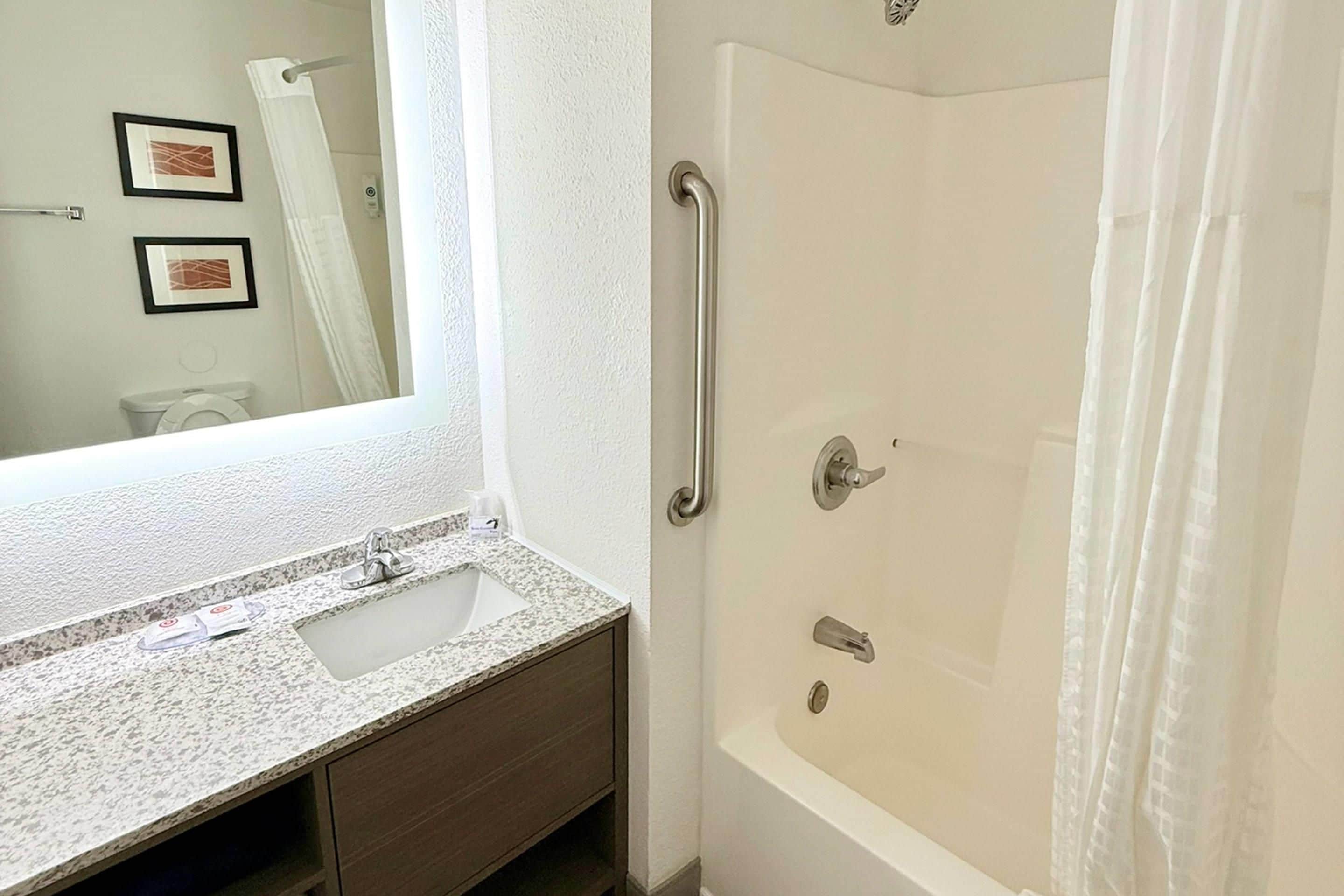 A bathroom with a sink, mirror, and a walk-in shower with a curtain.