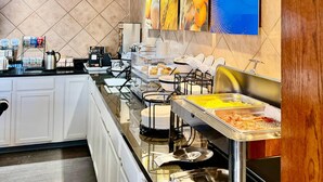 Ein reichhaltiges Buffet mit verschiedenen Speiseausgaben, darunter eine warme und eine kalte Theke, in einem modernen Küchenbereich mit gefliesten Wänden und einer glänzenden Arbeitsplatte.