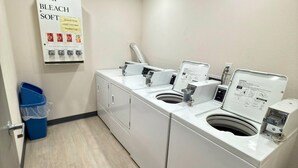 A laundry area with two washing machines, a soap and bleach dispenser, and a blue trash bin. - Comfort Inn Gallup I-40 Exit 20 (Gallup)