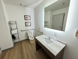 A modern bathroom with a white toilet, a sink with a granite countertop, a towel rack, and a mirror.