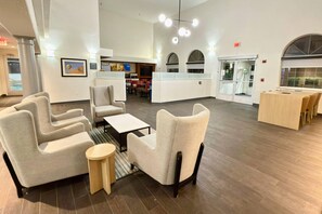A spacious lobby with modern furniture, a reception desk, and a view of the pool area.