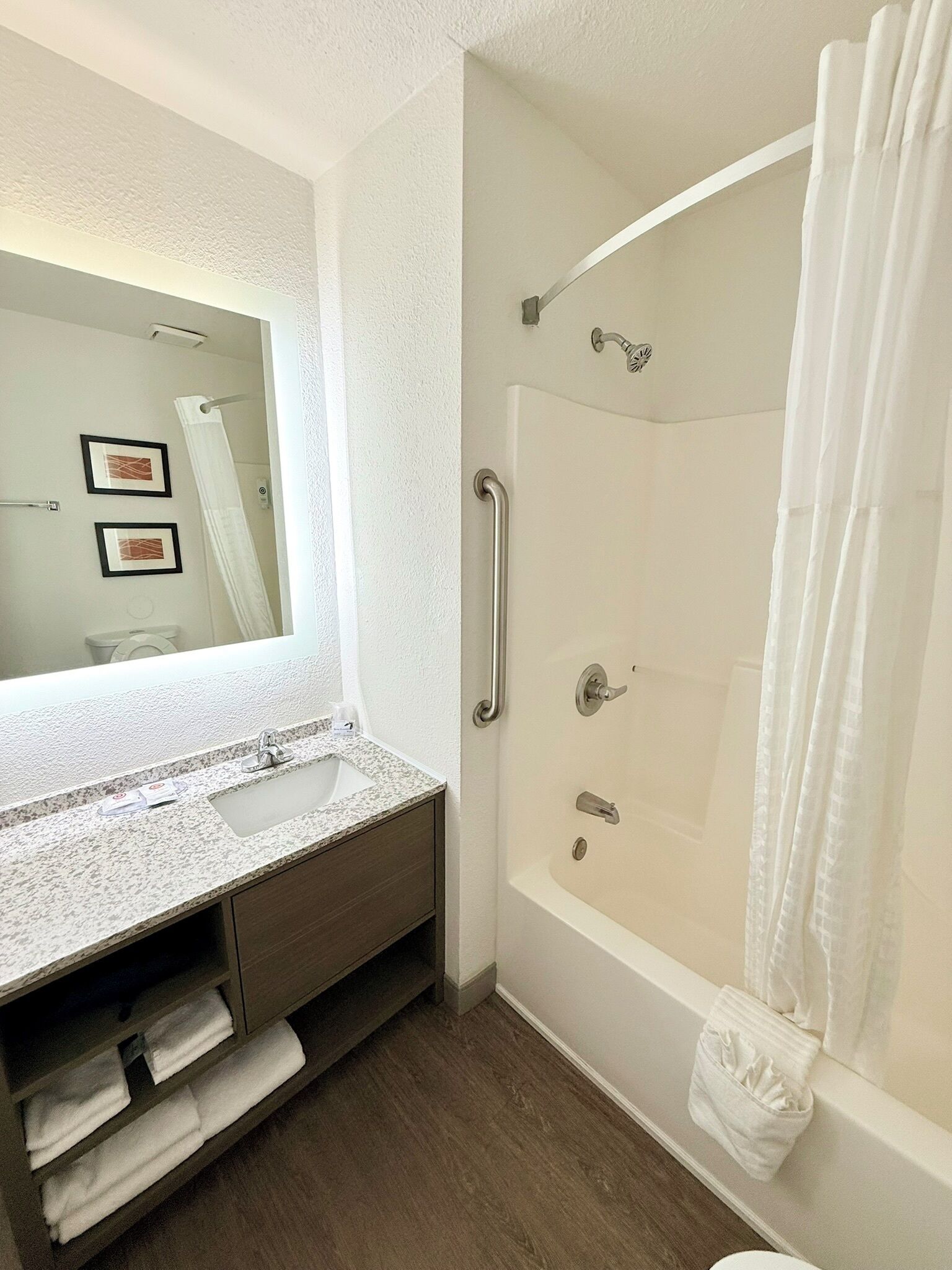 A modern bathroom with a large mirror, a granite countertop, a shower with a handheld showerhead, and a towel rack.