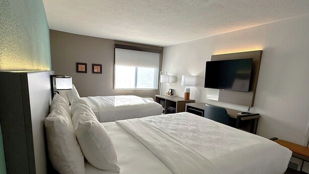 Ein Hotelzimmer mit zwei Betten, einem Schreibtisch, einem Fernseher und einem Fenster.