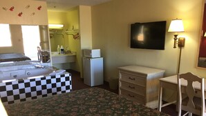 Habitació d'hotel amb un llit de quadres, una taula, una cadira, un televisor, un microones i un frigorífic.