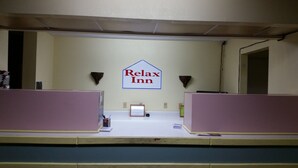 Una zona de recepció amb un cartell que diu 'Relax Inn', dos taulells de recepció i un petit certificat emmarcat al taulell.