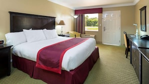 Quarto de hotel com uma cama grande, uma escrivaninha, uma cadeira, um abajur e uma porta para uma varanda.