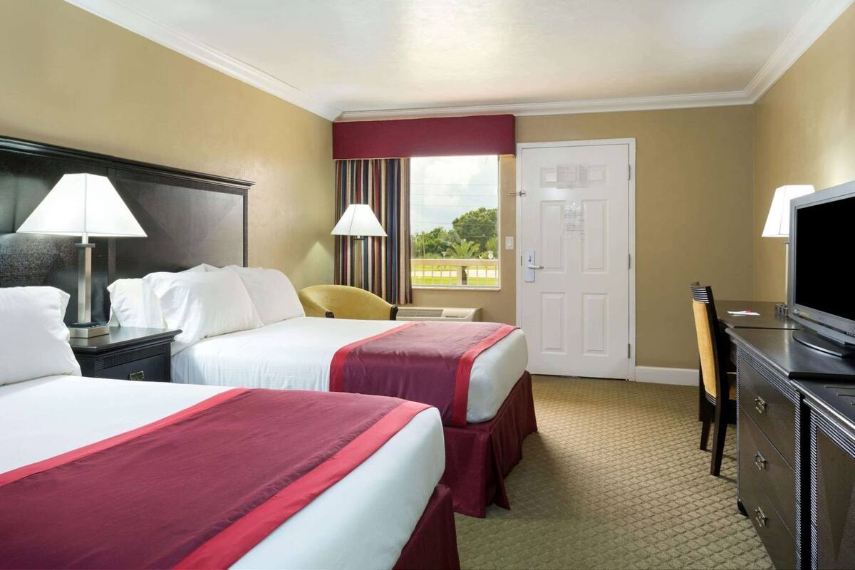 Habitación de hotel con dos camas, un escritorio, televisor y ventana con cortinas.