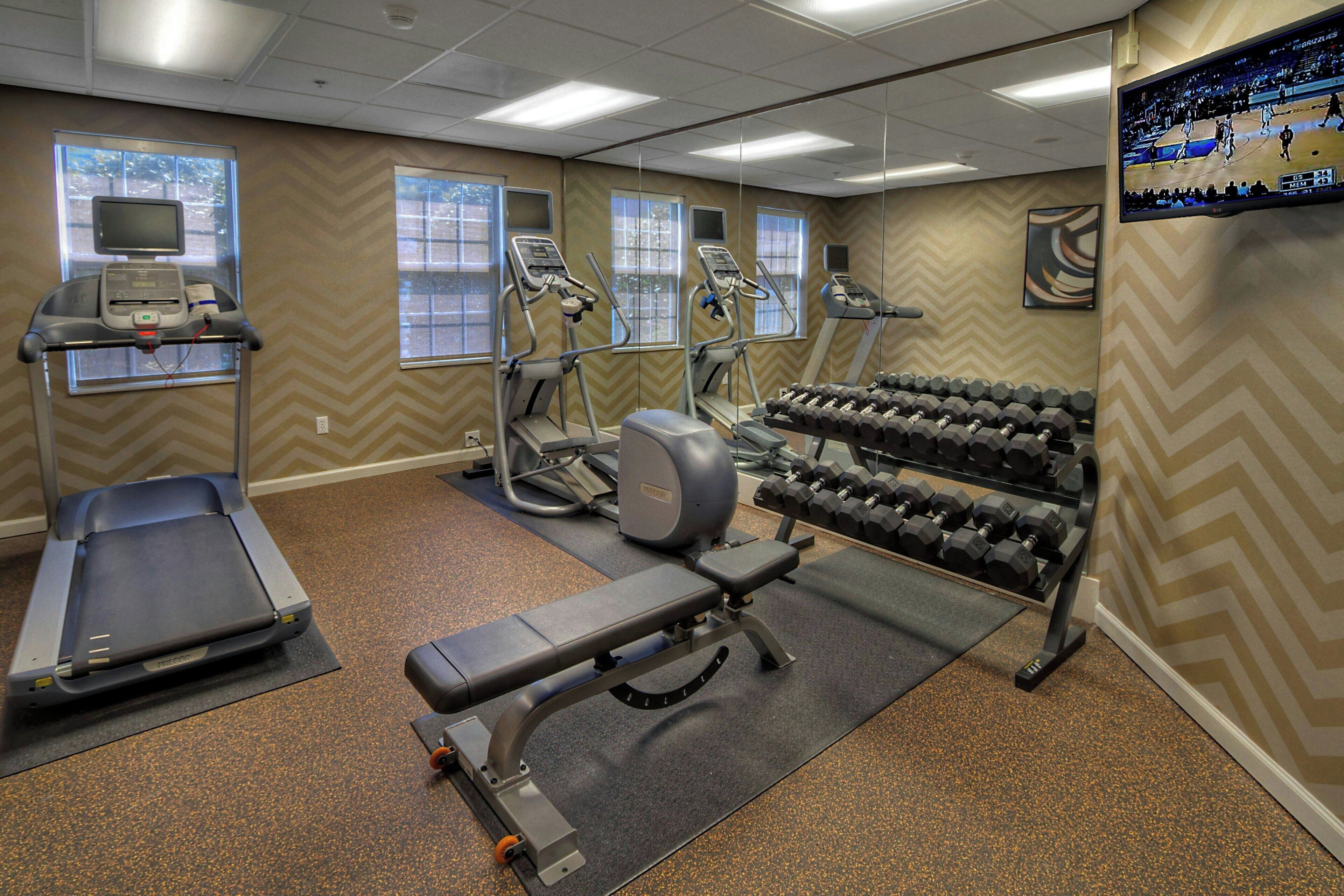Et fitnesscenter med løbebånd, crosstrainere, bænkpress og håndvægte.