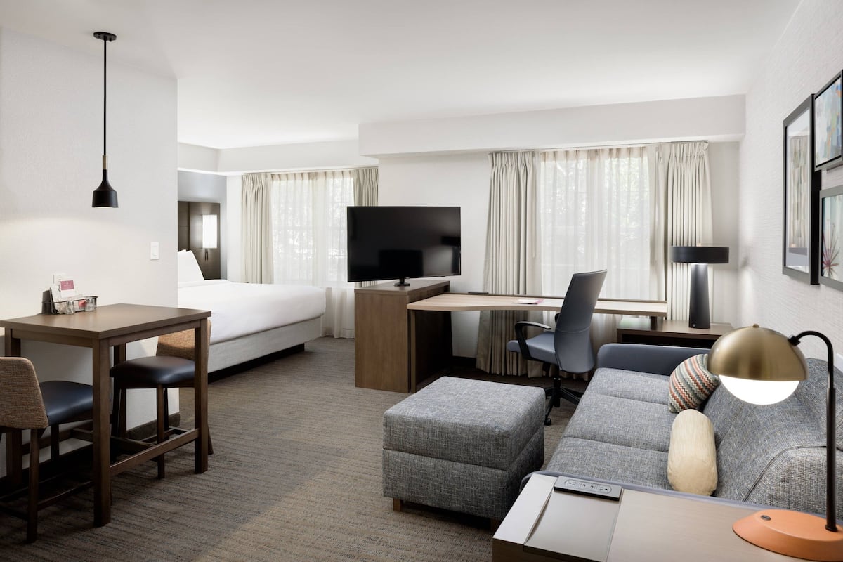 Una habitación de hotel con cama, escritorio con computadora, televisor, sofá y lámpara.