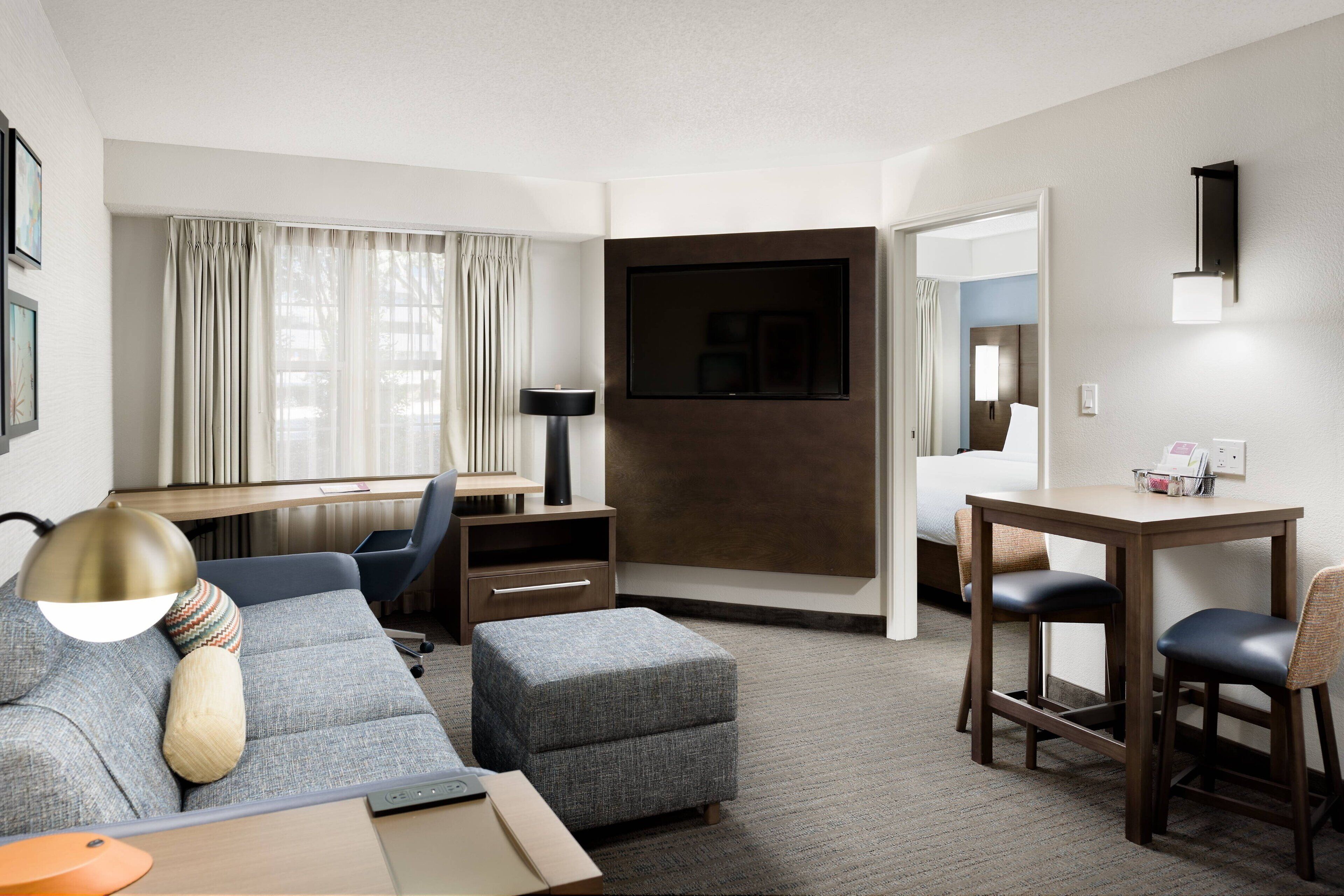 A modern hotel room with a sofa, ottoman, desk, and chairs.