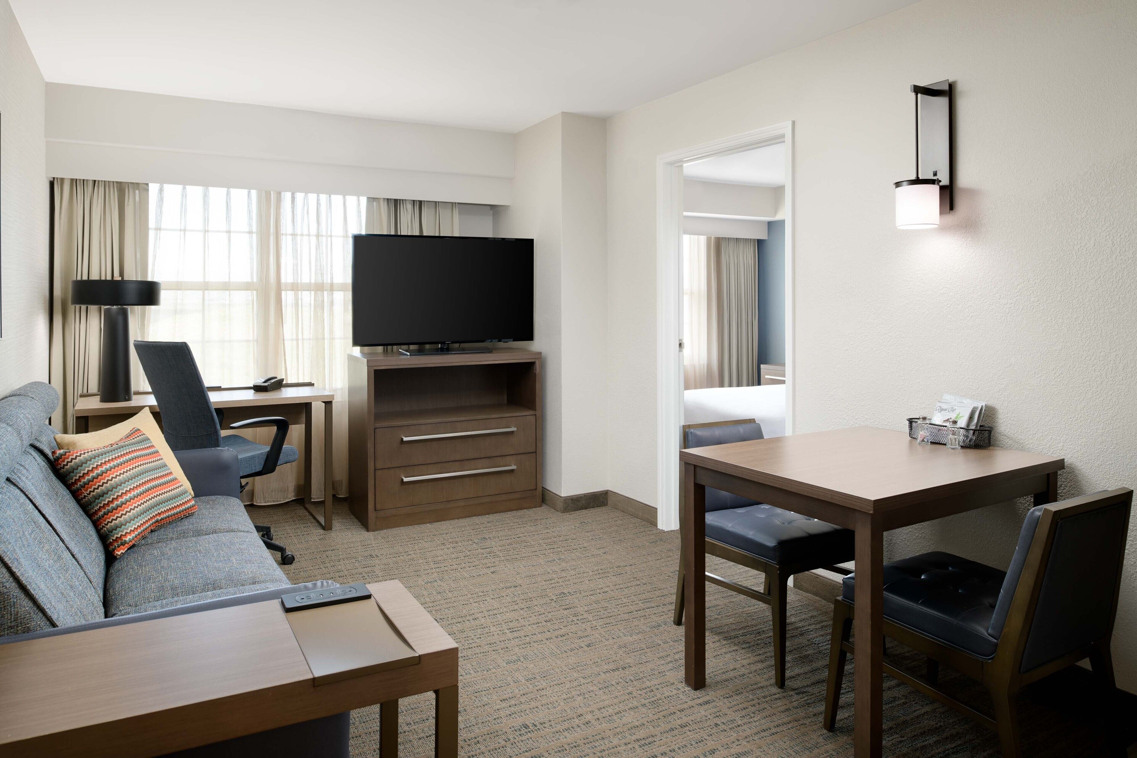 Habitación de hotel con sofá, escritorio con televisor, mesa de comedor y una silla.