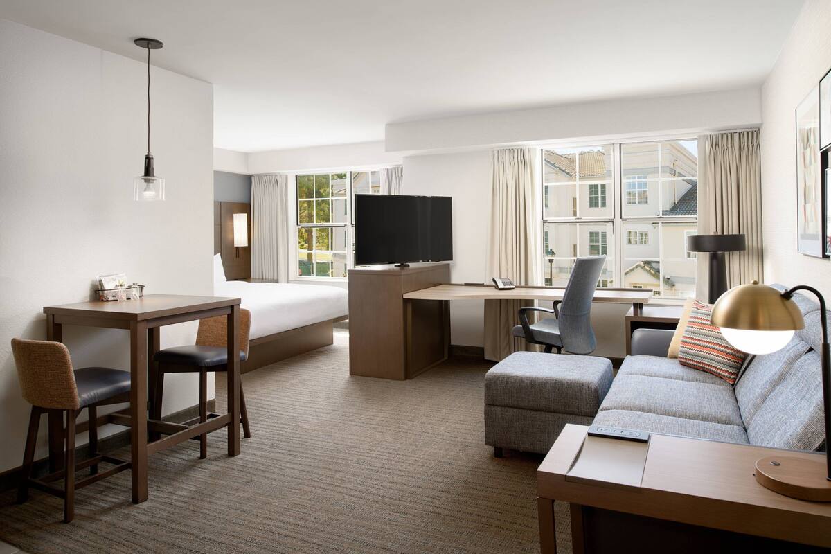Una habitación de hotel con cama, escritorio, televisor, sofá y sillas.