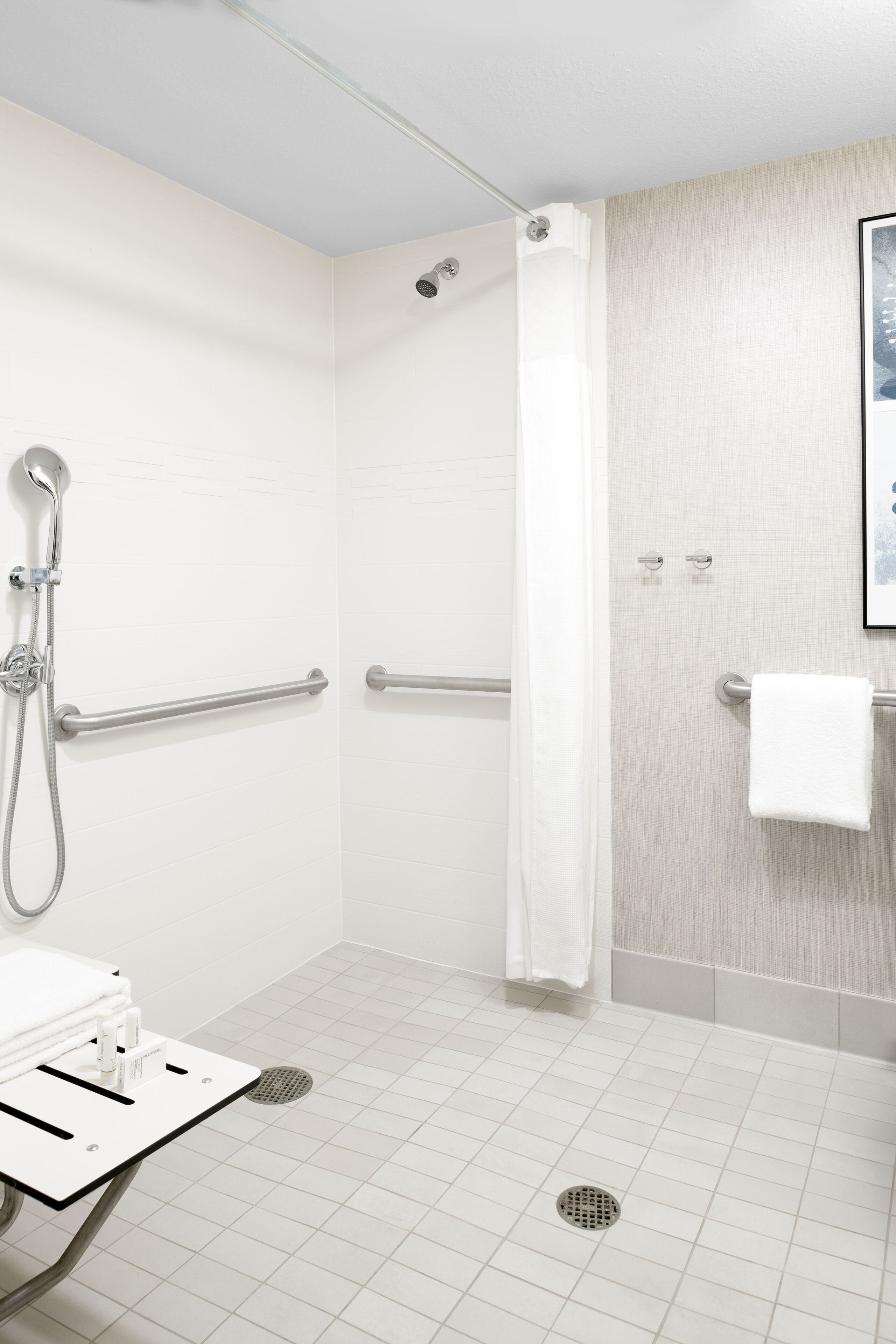 A modern bathroom with a walk-in shower, grab bars, a towel rack, and a sink with a mirror.