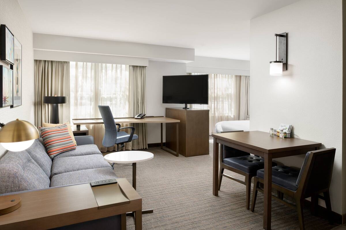 Habitación de hotel con sofá, mesa de comedor, televisor y escritorio.