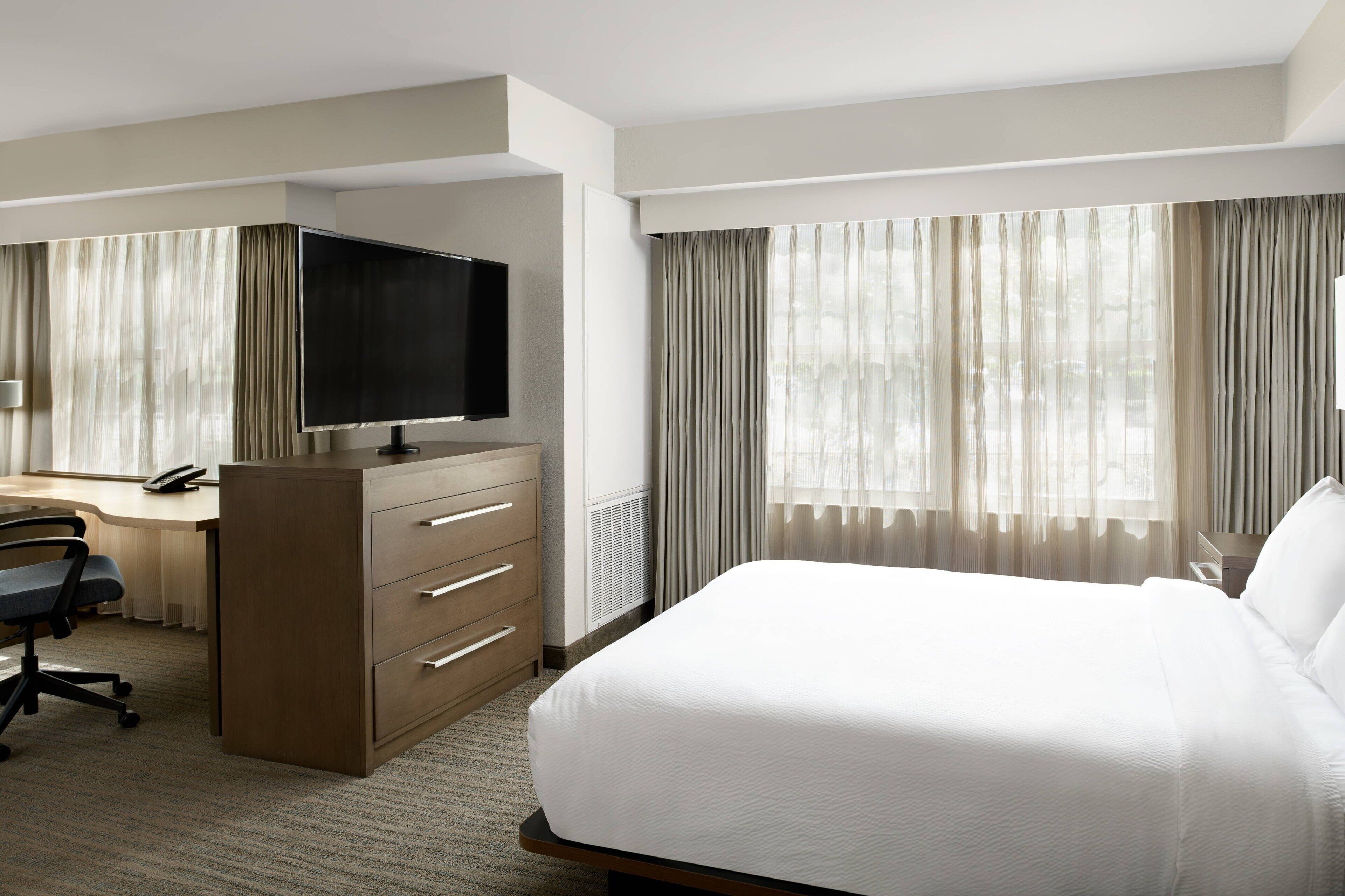 Ein Hotelzimmer mit Bett, Schreibtisch mit Stuhl, Fernseher und Kommode.