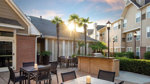 Eine Terrasse mit Sitzgelegenheit im Freien, einem Grill und Palmen.