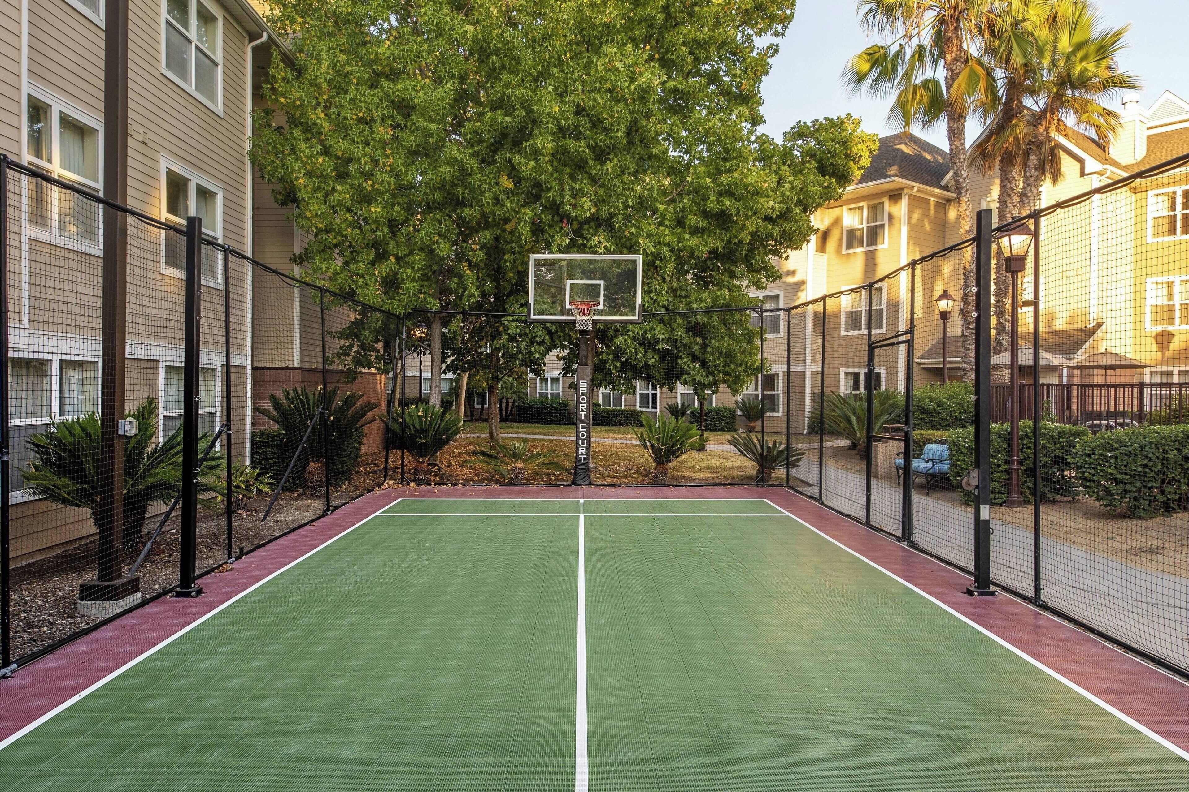Ein Basketballplatz im Freien, umgeben von Wohngebäuden, mit einem Basketballkorb in der Mitte.