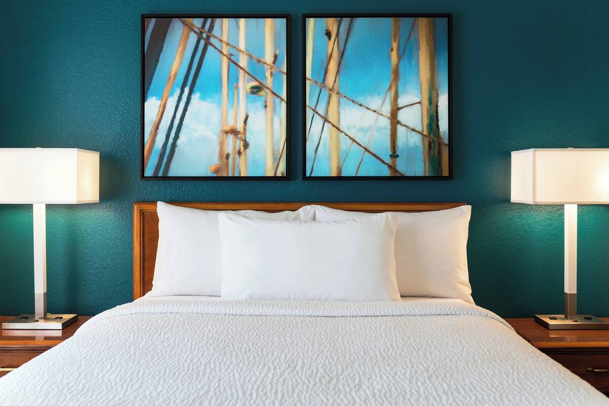 Ein Hotelzimmer mit einem Bett, zwei Wandgemälden und zwei Nachttischlampen.