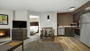 A modern hotel room with a flat-screen TV, a fireplace, a dining area with a table and chairs, a kitchen with a refrigerator and microwave, and a large window. - Residence Inn by Marriott Louisville Airport (Louisville)