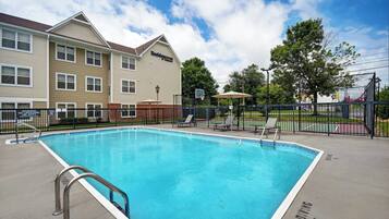 A swimming pool with a metal ladder, lounge chairs, and a basketball hoop.