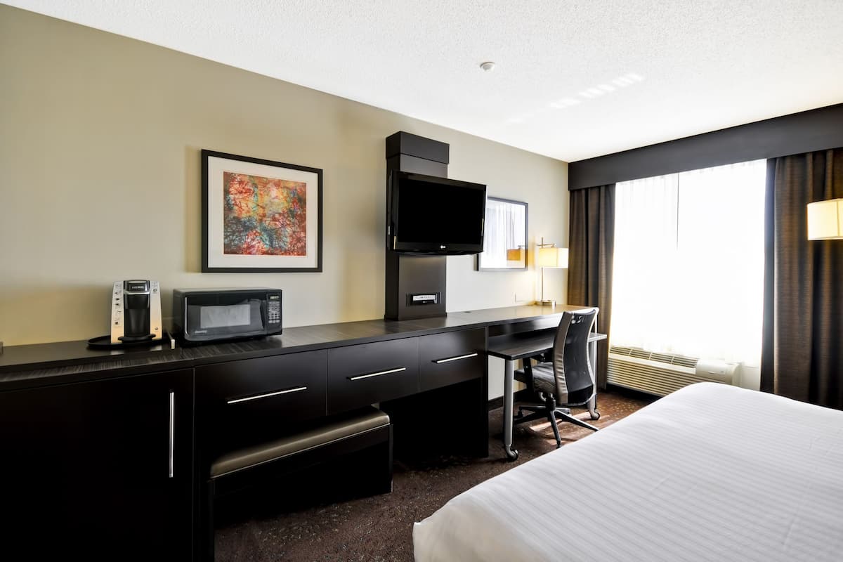 A hotel room with a bed, a desk with a flat-screen TV, a microwave, a coffee maker, and a chair.